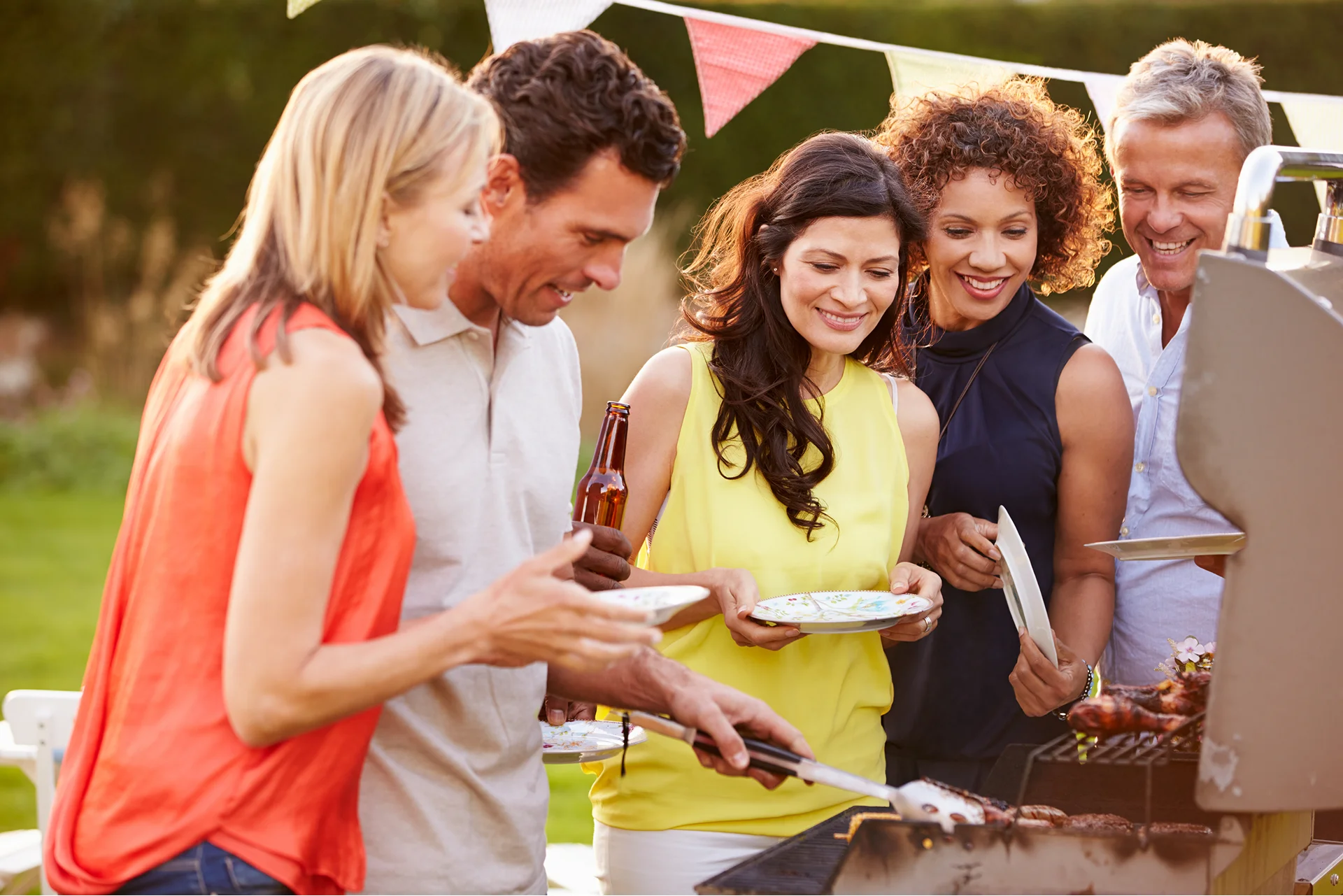 Five adults gather outdoors at Wildrye, grilling and sharing plates by new construction homes.