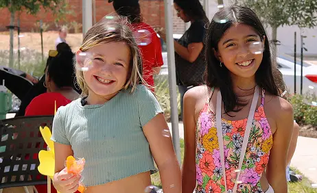 Two girls smiling outdoors by Wildrye new homes, surrounded by bubbles on a sunny day.